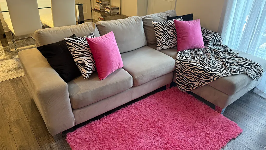 Pink, black, and zebra spa decor with a beige sofa, hot pink velvet pillows, black pillows, zebra-print pillows, and a pink rug.