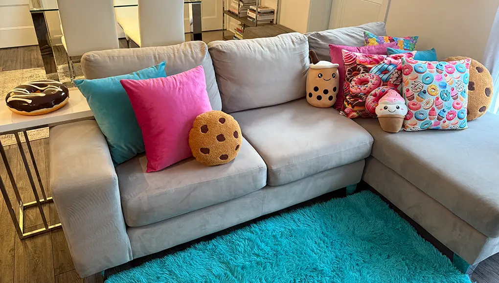 Sweets Spa Decor setup featuring a beige sectional sofa with aqua pillows, hot pink pillows, sweets-themed pillows, and an aqua carpet.