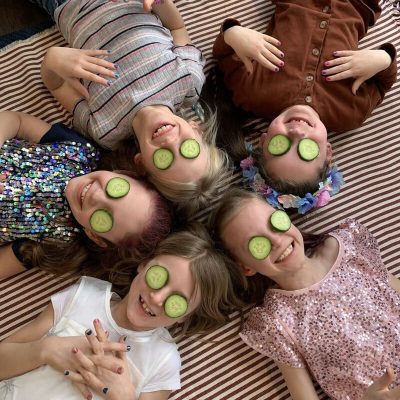 Kids lying on the floor smiling with sliced cucumbers on their eyes
