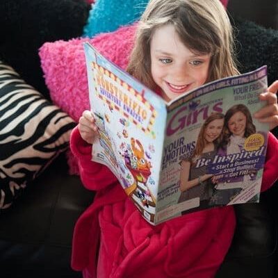 Cute girl wearing a pink Bath robe looking at a magazine